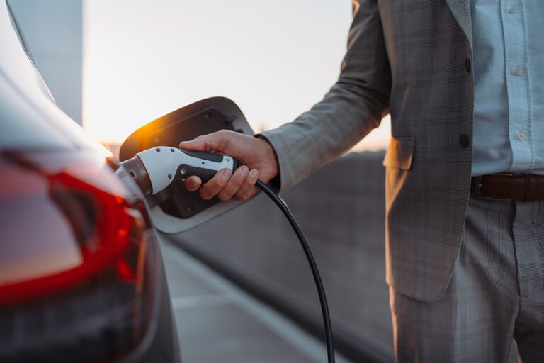 Man holding power supply cable at electric vehicle charging station, closeup