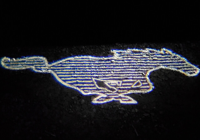 Electric Mustang logo on gravel from door's puddle light